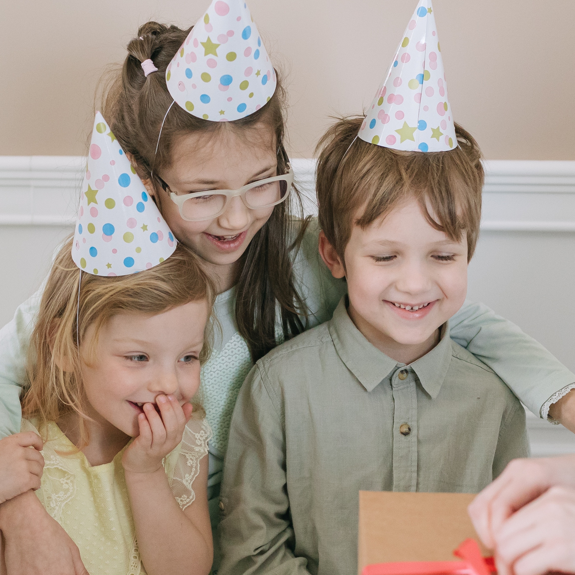 Tre bambini che guardano scartare un regalo con cappellini di carta in testa